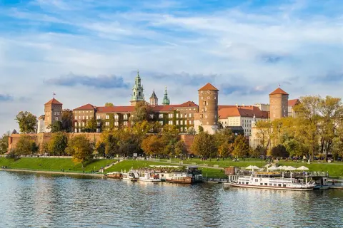 Zamek Królewski na Wawelu, majestatyczna budowla nad Wisłą, otoczona jesienną zielenią i błękitem nieba.