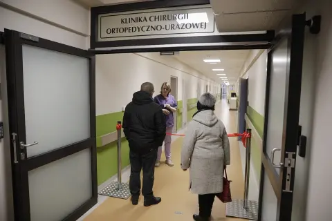 Korytarz szpitalny z tabliczką "Klinika Chirurgii Ortopedyczno-Urazowej", pacjenci i lekarka.