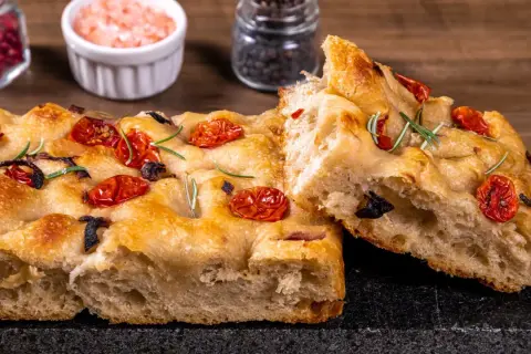 Złocista focaccia z pomidorkami koktajlowymi i rozmarynem, z widocznym puszystym wnętrzem.