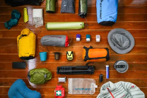A collection of gear for a backpacking trip: dry bags, sleeping pad, socks, hat, first aid kit, water bladder, and more.