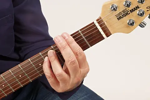 Gitarrenhals mit einem Finger, der einen Barre-Akkord greift. Der Zeigefinger liegt quer über alle Saiten.