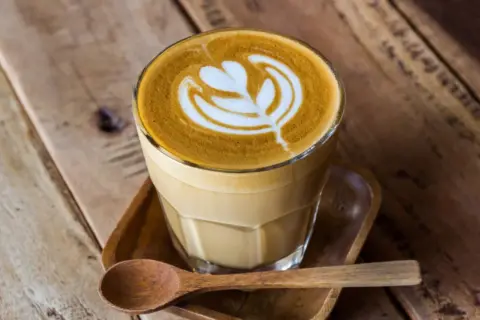 En vacker caffe latte med latte art på ett träbord. En träsked ligger bredvid.