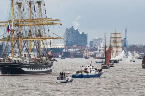 Große Segelschiffe und Dampfer nehmen an der einlaufparade hafengeburtstag teil, mit der Elbphilharmonie im Hintergrund.