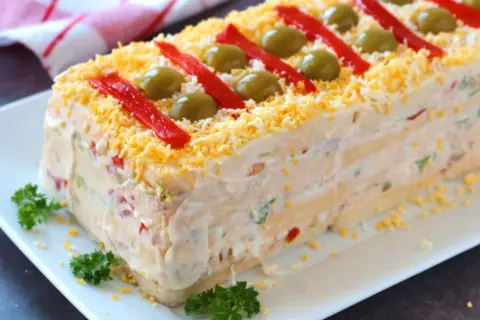 Pastel de atún con pan de molde, decorado con pimientos rojos, aceitunas y huevo rallado. ¡Una delicia!