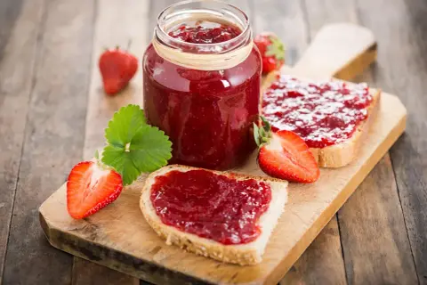 Confiture de fraises sur pain grillé, un délice qui peut faire grimper le cholestérol. Fraises fraîches et une feuille verte sur fond de bois.