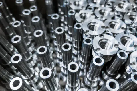 Metalowe elementy, precyzyjnie wykonane przez toczenie CNC, tworzą gęsty wzór. Widać gwintowane części i cylindryczne detale.