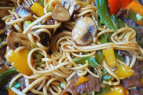 Pyszny makaron chow mein z wołowiną, pieczarkami, papryką i groszkiem cukrowym w sosie.