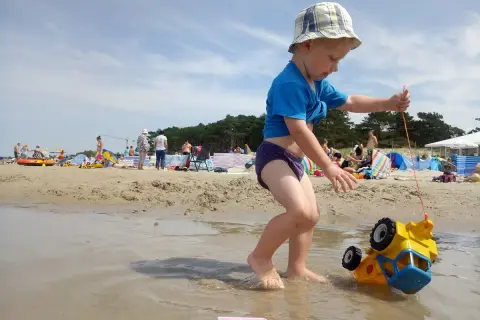 Chłopiec ciągnie zabawkowe auto po plaży w Darłowie. To świetne darłowo atrakcje dla dzieci, gdzie można się bawić w wodzie i piasku.