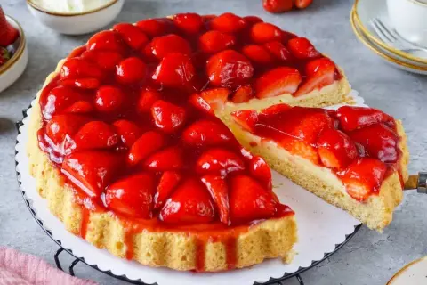 Eine saftige Erdbeertorte mit frischen Erdbeeren und Tortenguss, ein Stück wird herausgeschnitten.