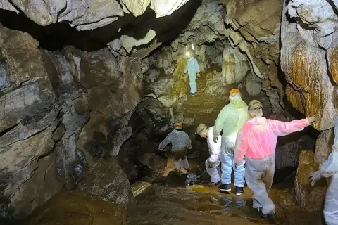 Exploradores descienden en la Cova do Rei Cintolo, iluminando formaciones rocosas y charcos de agua.