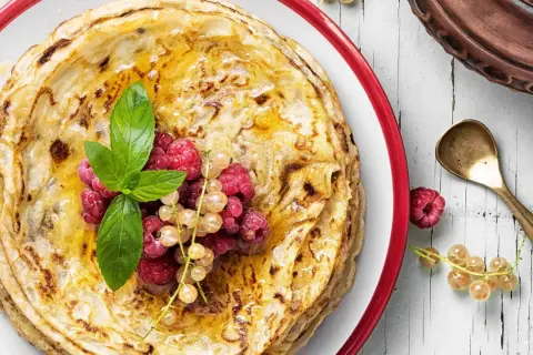 Gestapelte Pfannkuchen ohne Mehl, beträufelt mit Honig und garniert mit frischen Beeren und Minze. Ein köstlicher Genuss!