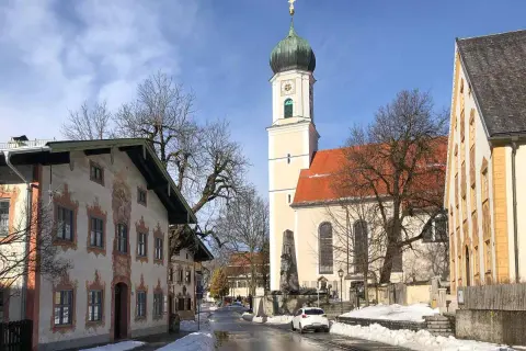 Winterliche Szene in Oberammergau mit der Pfarrkirche St. Peter und Paul. Die Fassadenmalerei der Häuser und die schneebedeckten Wege lassen die Vorfreude auf die passionsfestspiele oberammergau spüren.