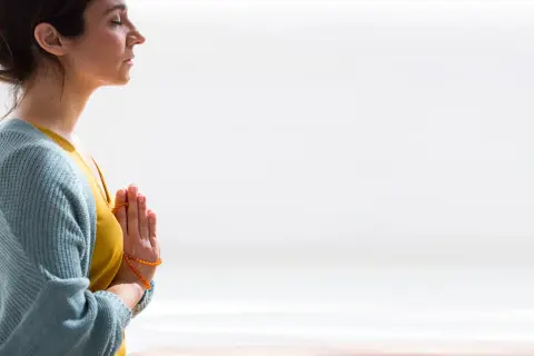 Mujer meditando con las manos juntas en posición de oración, reflejando el namasté significado yoga.