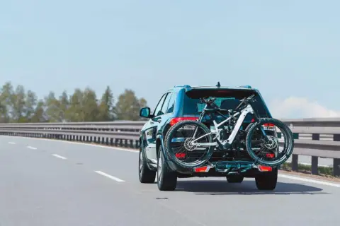 Un turismo transporta una bicicleta de montaña en un portabicicletas trasero. La carga sobresale considerablemente, pero es una forma común de llevar equipo deportivo.