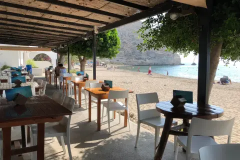 Mesas y sillas en el exterior del restaurante Agua Amarga, con la playa y el mar de fondo.