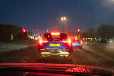 Noche de nieve, luces rojas de freno y un coche azul con matrícula amarilla. El asfalto mojado y la baja visibilidad aumentan el riesgo de derrape coche.
