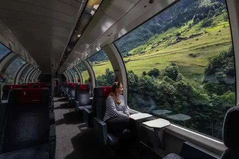 Kobieta podziwia alpejskie krajobrazy ze szwajcarskiego pociągu panoramicznego. Cena biletu jest adekwatna do widoków.