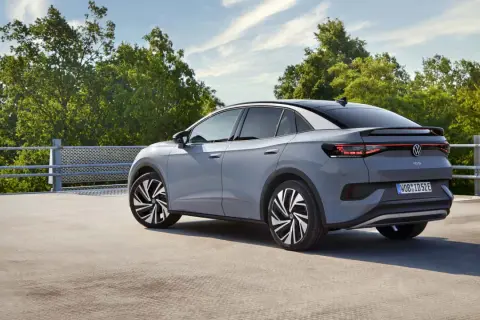 El Volkswagen ID.5 gris, con su diseño deportivo, se detiene en un día soleado, rodeado de árboles verdes y un cielo azul.