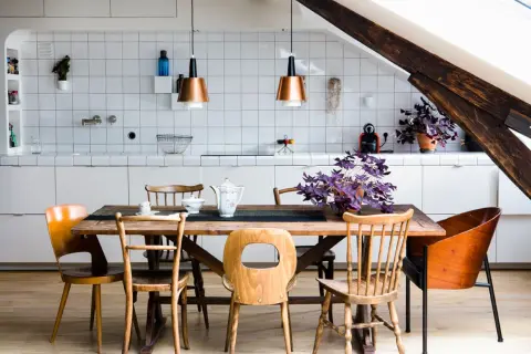 Une cuisine ouverte en L avec un îlot central en bois, des chaises vintage et des suspensions cuivrées. Une plante violette apporte une touche de couleur.