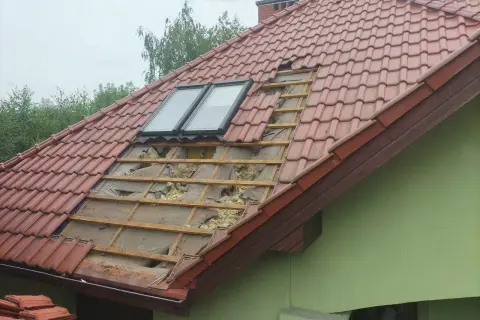 Uszkodzony dach z dachówką, widoczne okna dachowe i izolacja. Czas pomyśleć, jak uszczelnić dach przed kunami.