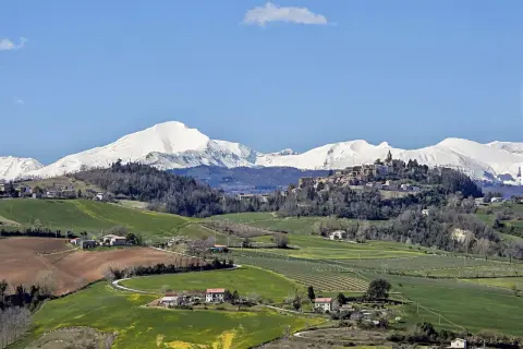 Paesaggio collinare con un borgo in cima, montagne innevate sullo sfondo. Un tranquillo scorcio del fermo provincia.