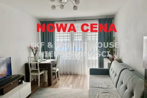 Nowa cena nieruchomości! Salon z jadalnią, kanapą i stołem. Okna z zasłonami.