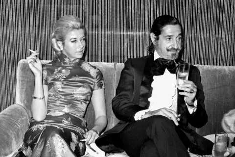 Jaime de Mora y Aragón, elegante en esmoquin, brinda con una copa mientras una mujer con vestido oriental fuma.