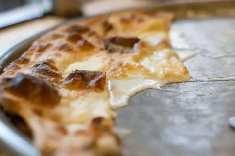 En bit av en gyllene focaccia di Recco med smält ost som rinner ut på en plåt.