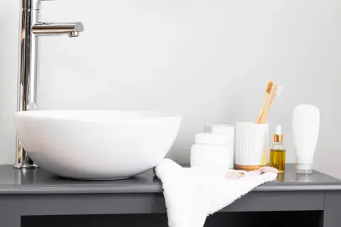 Elegancka umywalka nablatowa 50 z chromowaną baterią, obok kosmetyki i bambusowe szczoteczki do zębów.