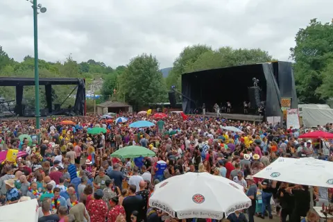 Multitud disfrutando de un concierto al aire libre en Naseiro, Viveiro. Gente bailando y animando bajo un cielo nublado.