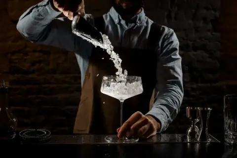 Barman aggiunge ghiaccio tritato in un calice. La corretta temperatura frigo bar bevande è fondamentale per un cocktail perfetto.