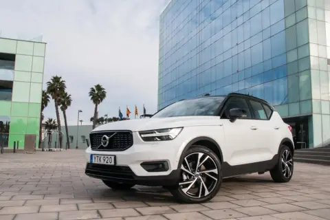 Białe Volvo XC40 z czarnym dachem zaparkowane przed nowoczesnym budynkiem z niebieskimi oknami.