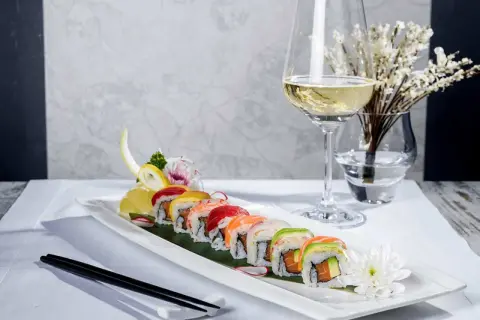 En elegant uppsättning sushirullar med färgglada toppingar, serverade med en glas vin till sushi. En vacker dukning med blommor och ätpinnar.