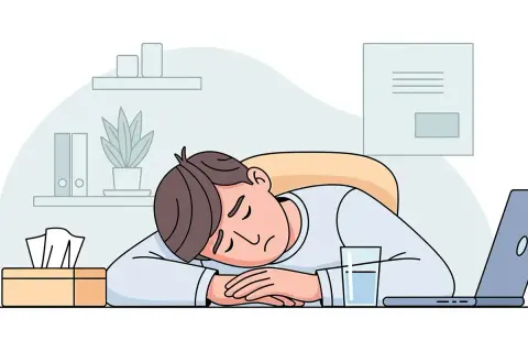 Ein Mann schläft erschöpft auf seinem Schreibtisch ein, ein Glas Wasser und Taschentücher daneben. Ein Bild für stillen Burnout.