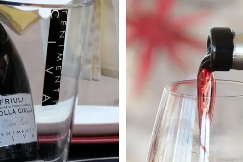 Un bicchiere si riempie di vino rosso, mostrando come si versa il vino. A sinistra, una bottiglia di Ribolla Gialla è in un secchiello.