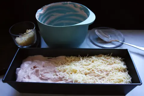 Förberedelser för ett gott kassler recept: en form med kassler och ost, en skål med riven ost och en tom blandskål.