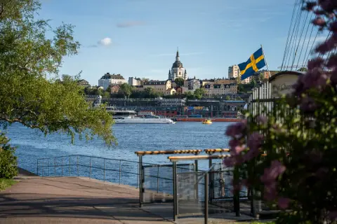 Ein perfekter Blick auf Stockholm für Ihr 4 Tage Stockholm Programm: Die Skyline mit Kirche, die schwedische Flagge und ein Boot auf dem Wasser.