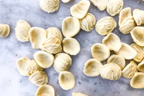 Orecchiette, die "kleinen Ohren" der Pasta, liegen auf grauem Marmor. Die Aussprache ist einfach: Oh-reck-ee-ette.