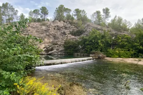 La source du Lez, une cascade artificielle sur une rivière bordée de falaises rocheuses et de végétation luxuriante.