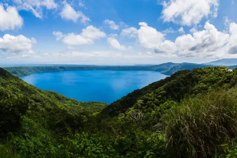 Vista panorámica de un lago azul intenso rodeado de vegetación exuberante y montañas. Un destino imperdible que ver en Nicaragua.