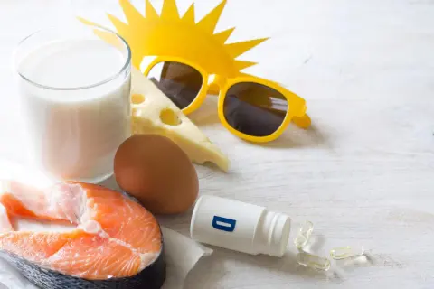 Zomerse zon, zonnebril en voedingsmiddelen die een stootkuur vitamine D bieden: zalm, ei, melk en kaas. Ook supplementen zijn zichtbaar.