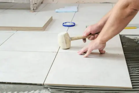 Pose de carrelage sans plinthe, un artisan ajuste une dalle avec un maillet en caoutchouc sur le mortier frais.