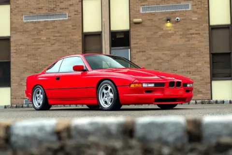 Czerwone BMW serii 8 (E50) z lat 90. zaparkowane przed budynkiem z cegły.