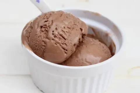 Dos bolas de cremoso helado de chocolate casero en un cuenco blanco, con una cuchara lista para disfrutar.