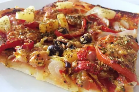En bit pizza med ananas, oliver och paprika. Ett perfekt glutenfri pizzadeg recept för en god middag.