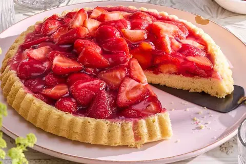 Ein saftiger Erdbeerkuchen, frisch belegt mit vielen roten Erdbeeren und glänzendem Tortenguss. Ein Stück ist bereits herausgeschnitten.