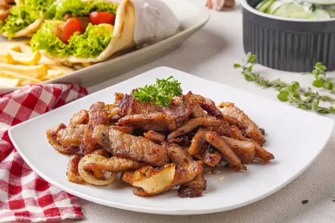 Saftiges Fleisch für ein köstliches Gyros Rezept, garniert mit Petersilie. Daneben liegen Gyros-Wraps und ein Gurkensalat.