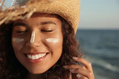 Mujer sonríe con protector solar en la cara, protegiéndose de la elastosis solar.