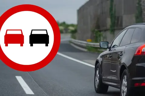 Znak zakazu wyprzedzania na podwójnej ciągłej. Czarny SUV jedzie po drodze, a na pierwszym planie znak drogowy.