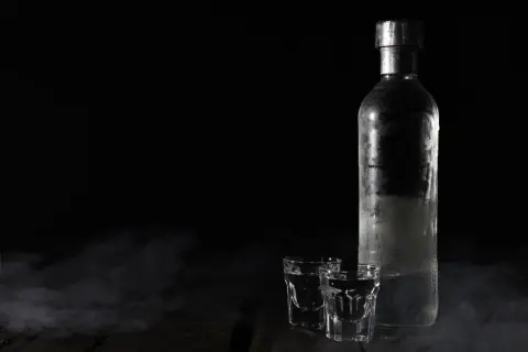 Chłodna butelka wódki i dwa kieliszki na ciemnym tle. Zastanawiasz się, jak długo może stać otwarta wódka?